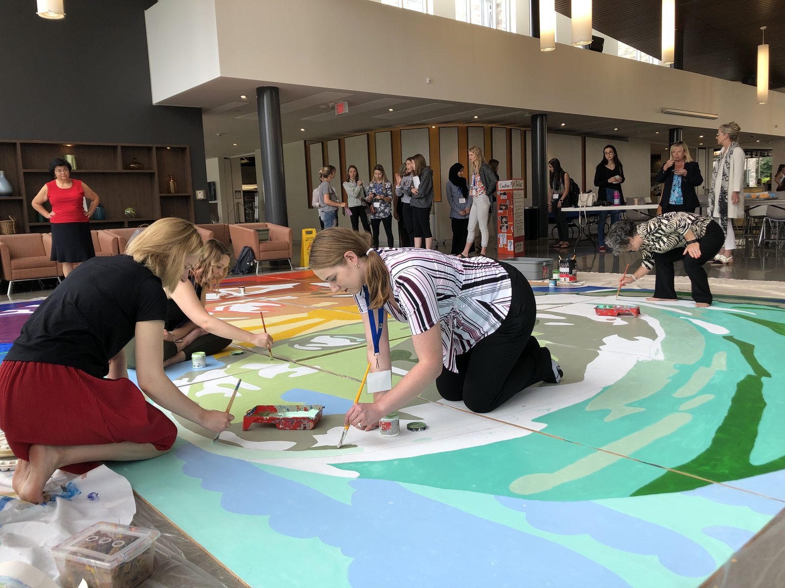 Staff and students painting a large mural canvas on the floor of a bright university atrium