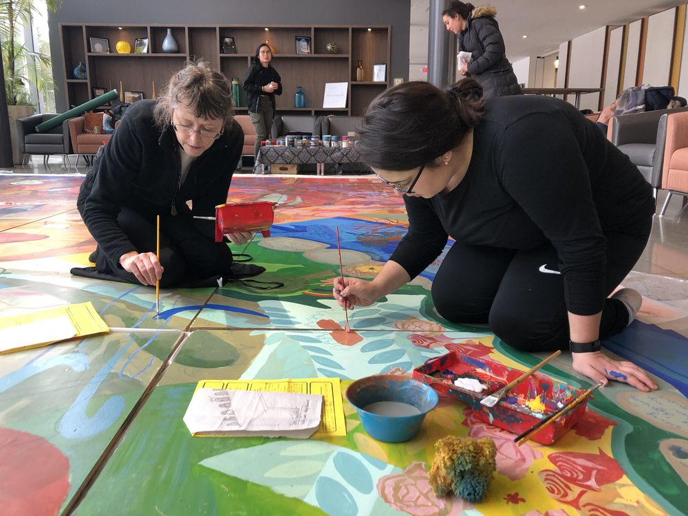 Two people painting side by side on the floor