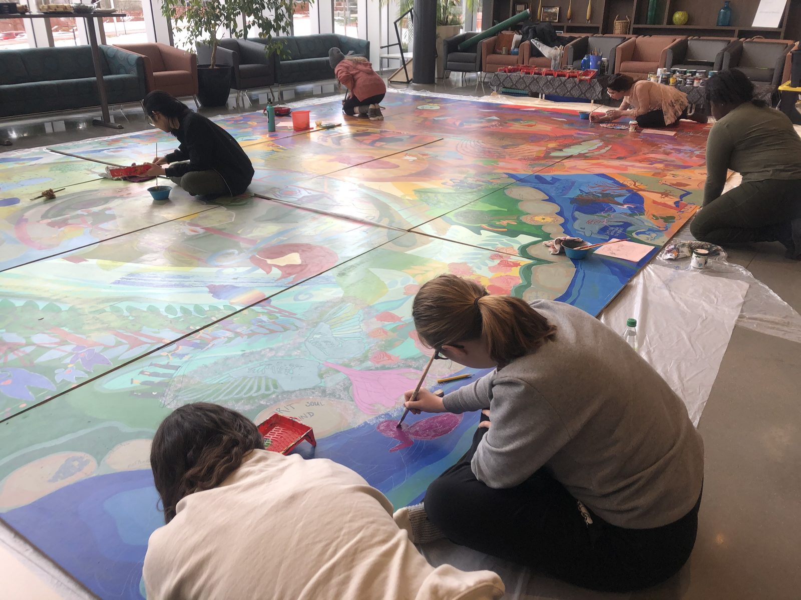 Staff and students painting a large shared canvas together on the floor